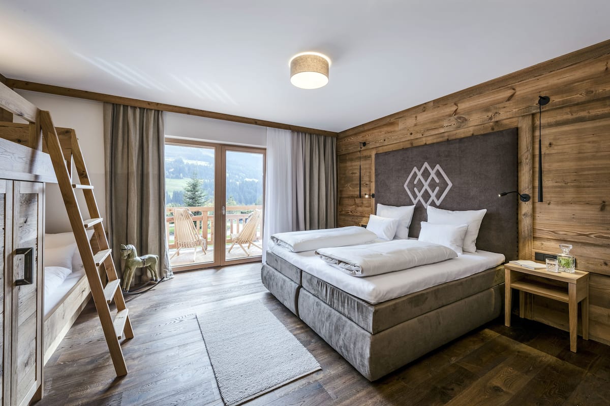 Un dormitorio con cama, paredes de madera, una escalera, una mesita de noche y vistas al exterior.