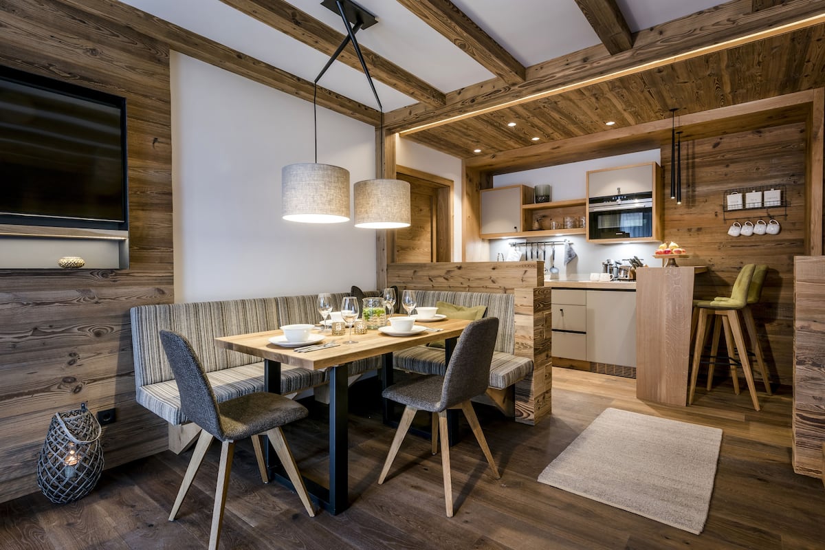 Una cocina moderna con vigas de madera, un comedor con mesa y sillas, y un horno empotrado.