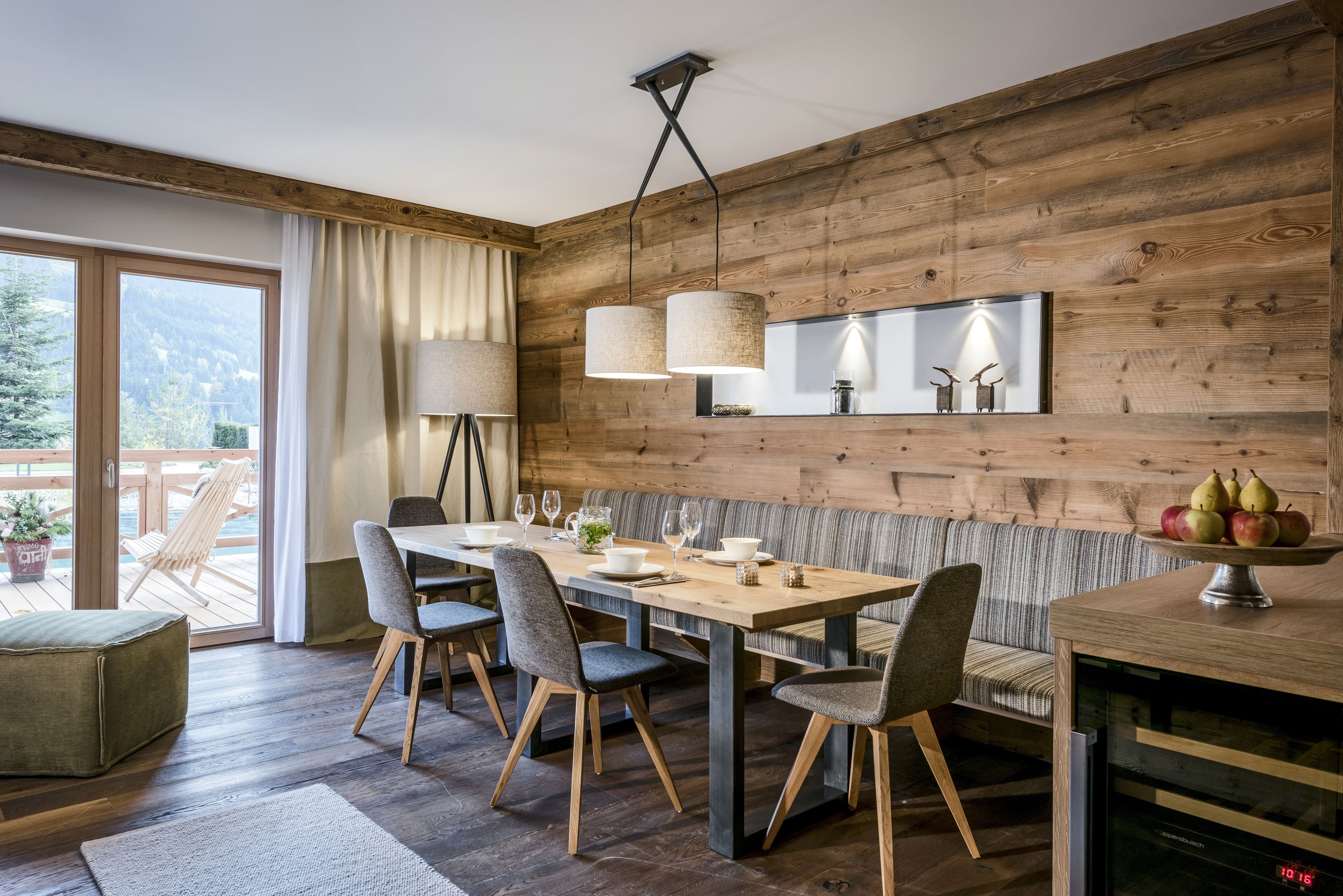 Comedor con pared de madera, un amplio ventanal y una mesa preparada para cuatro.