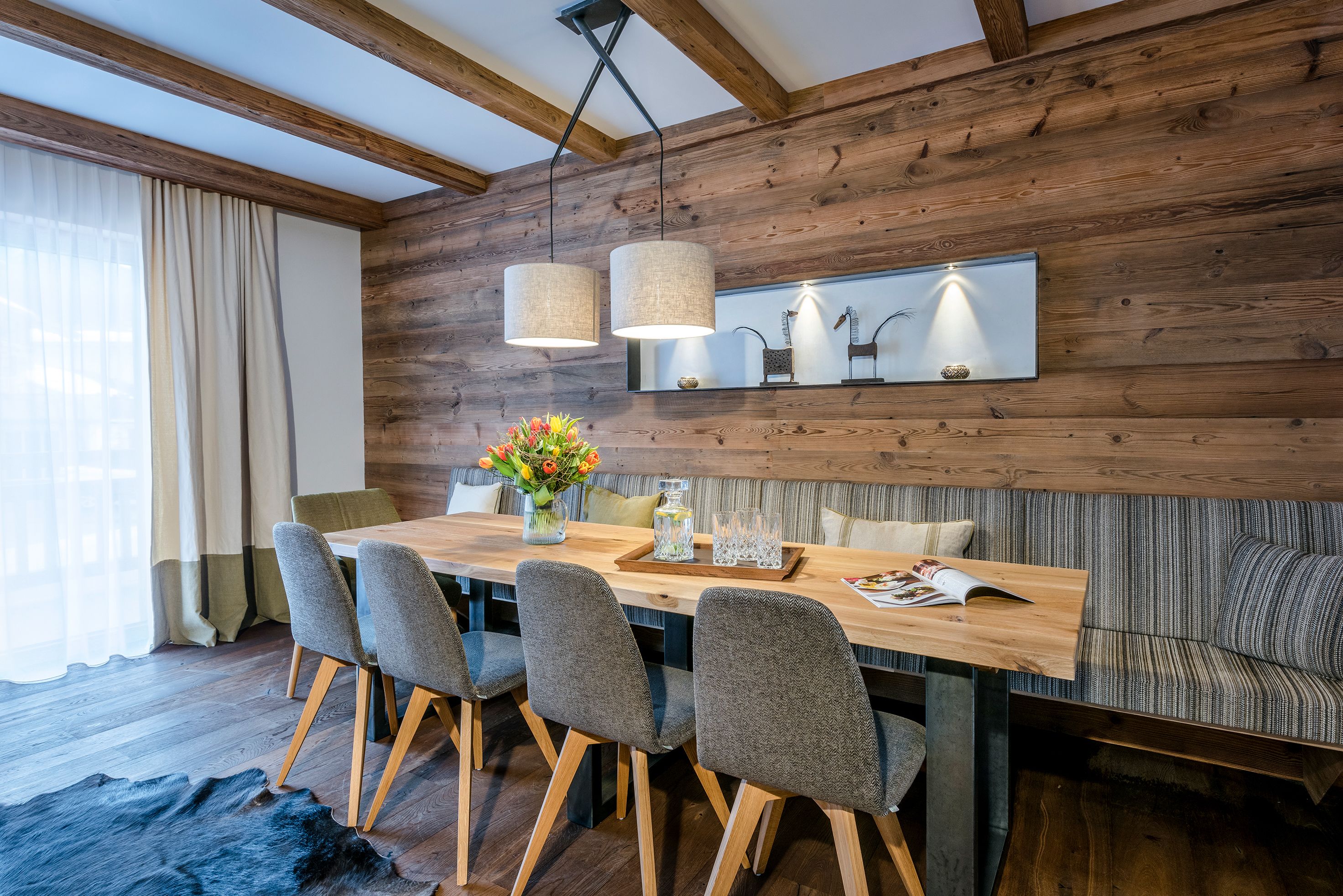 A modern dining area with a wooden table, grey upholstered chairs, and a bench.