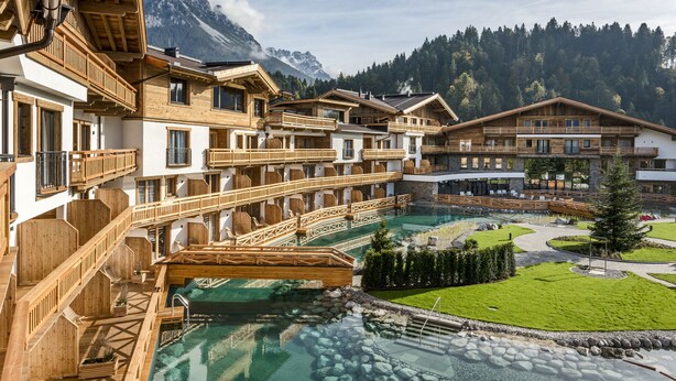 Un complexe hôtelier doté de nombreux balcons en bois, d’une piscine centrale à l’eau claire et surplombant un paysage montagneux.