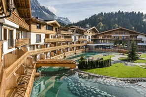 Un complexe hôtelier doté de nombreux balcons en bois, d’une piscine centrale à l’eau claire et surplombant un paysage montagneux.