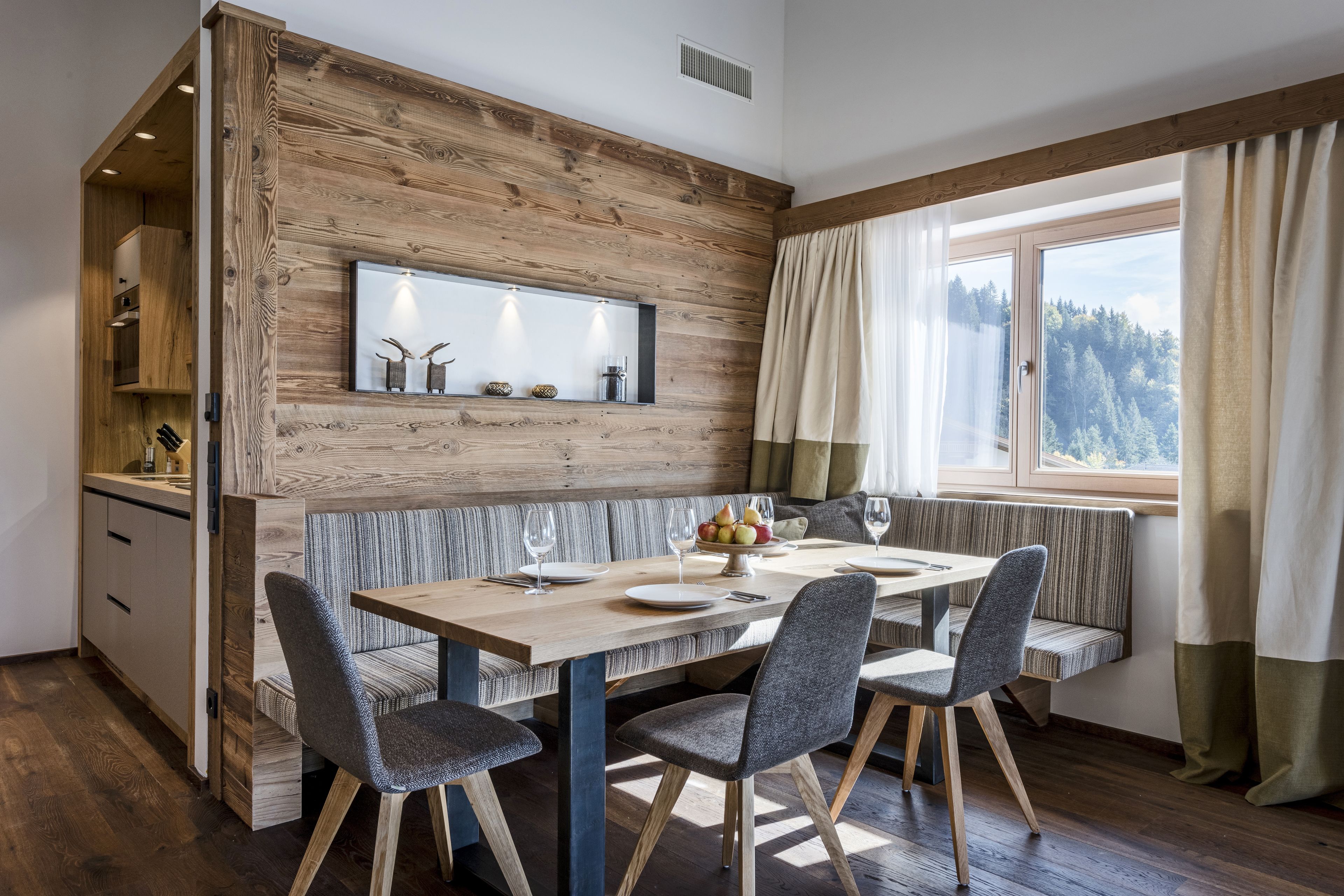 A dining area with a wooden wall, a window with curtains, and a bench seating area.