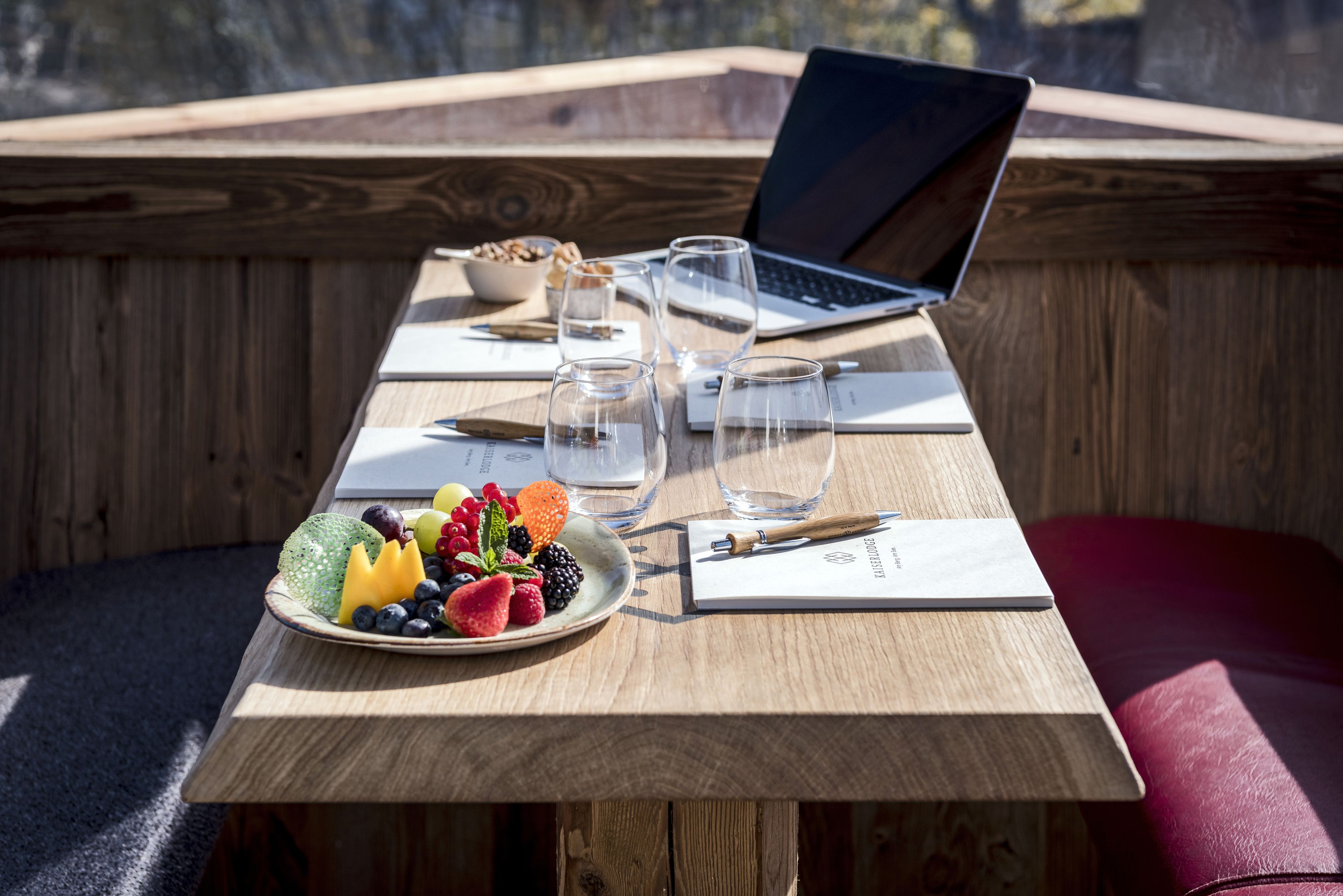 Una mesa de madera con una computadora portátil, gafas, un plato de fruta y un cuaderno.