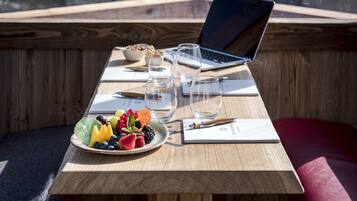 Una mesa de madera con una computadora portátil, gafas, un plato de fruta y un cuaderno.