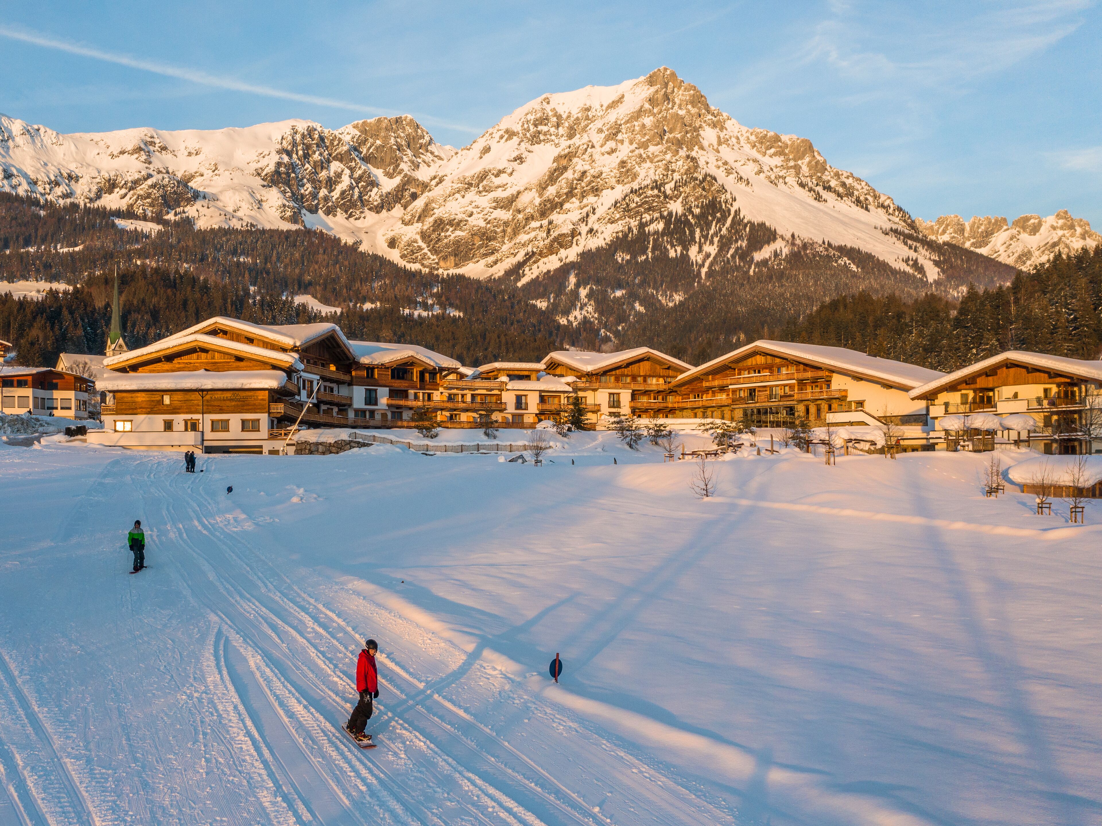 A ski resort with multiple chalet-style buildings, ski slopes, and snow-covered mountains in the background.