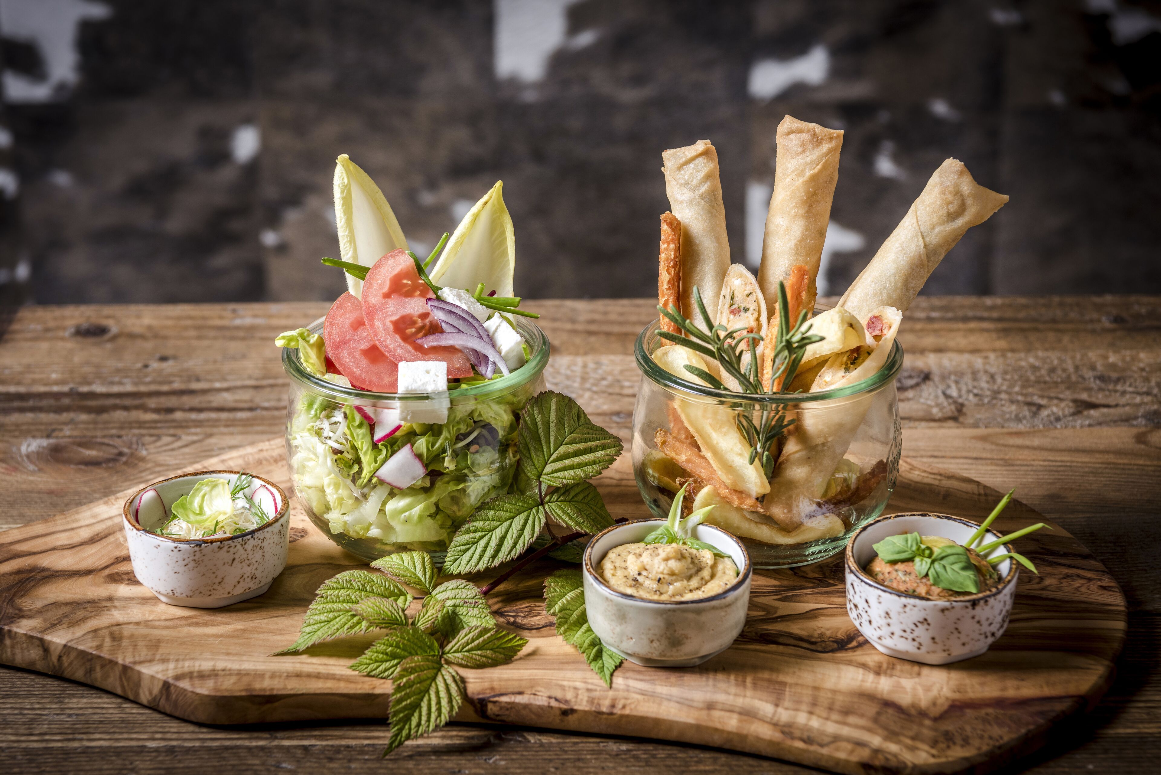 Two glass jars with food items, a wooden board with bowls, and mint leaves.