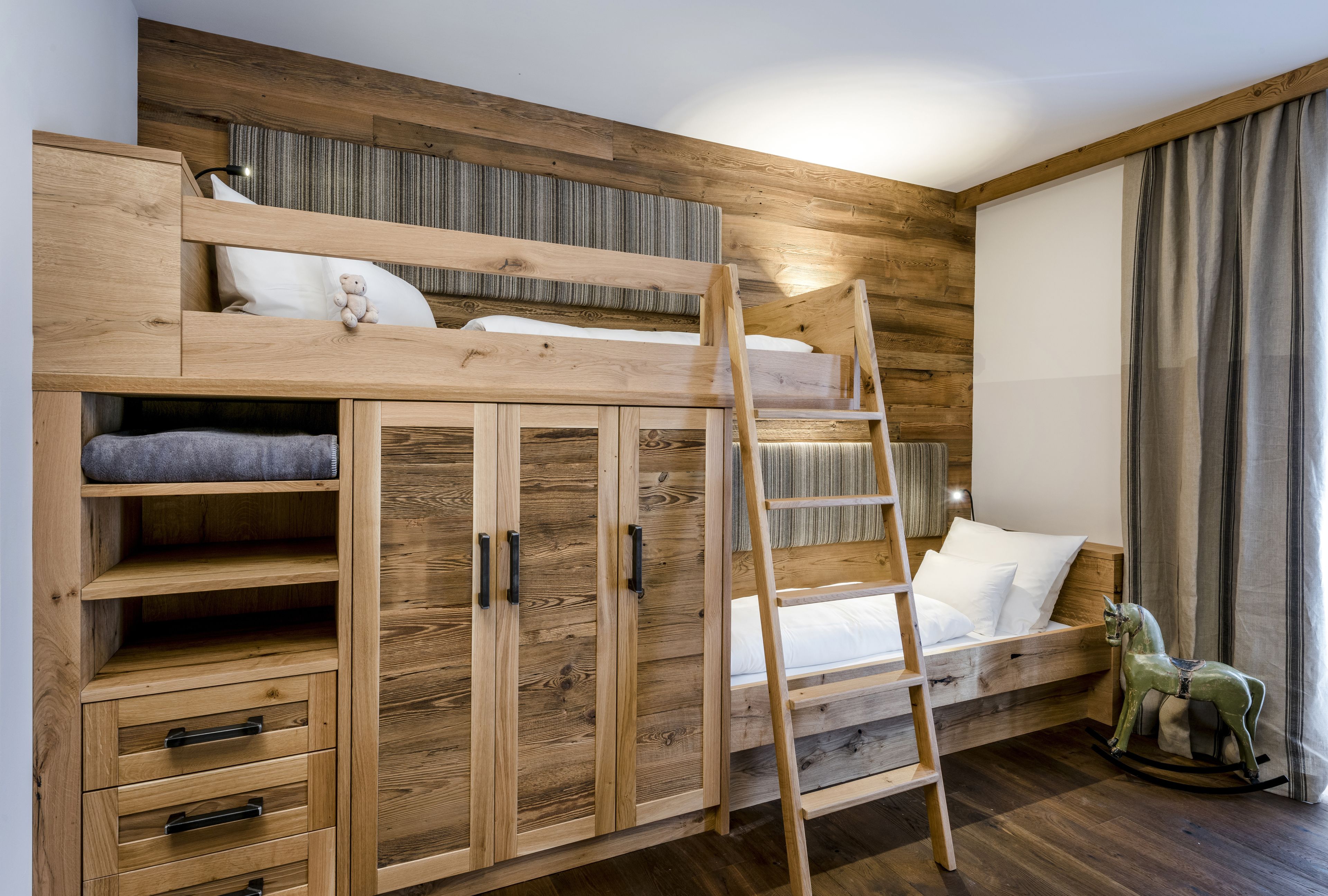 Een stapelbed met een ladder, een houten garderobe en een schommelpaard.