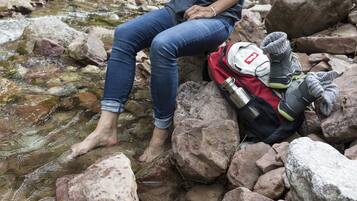 Eine Person sitzt auf Felsen an einem Bach, trägt Jeans und eine Armbanduhr.