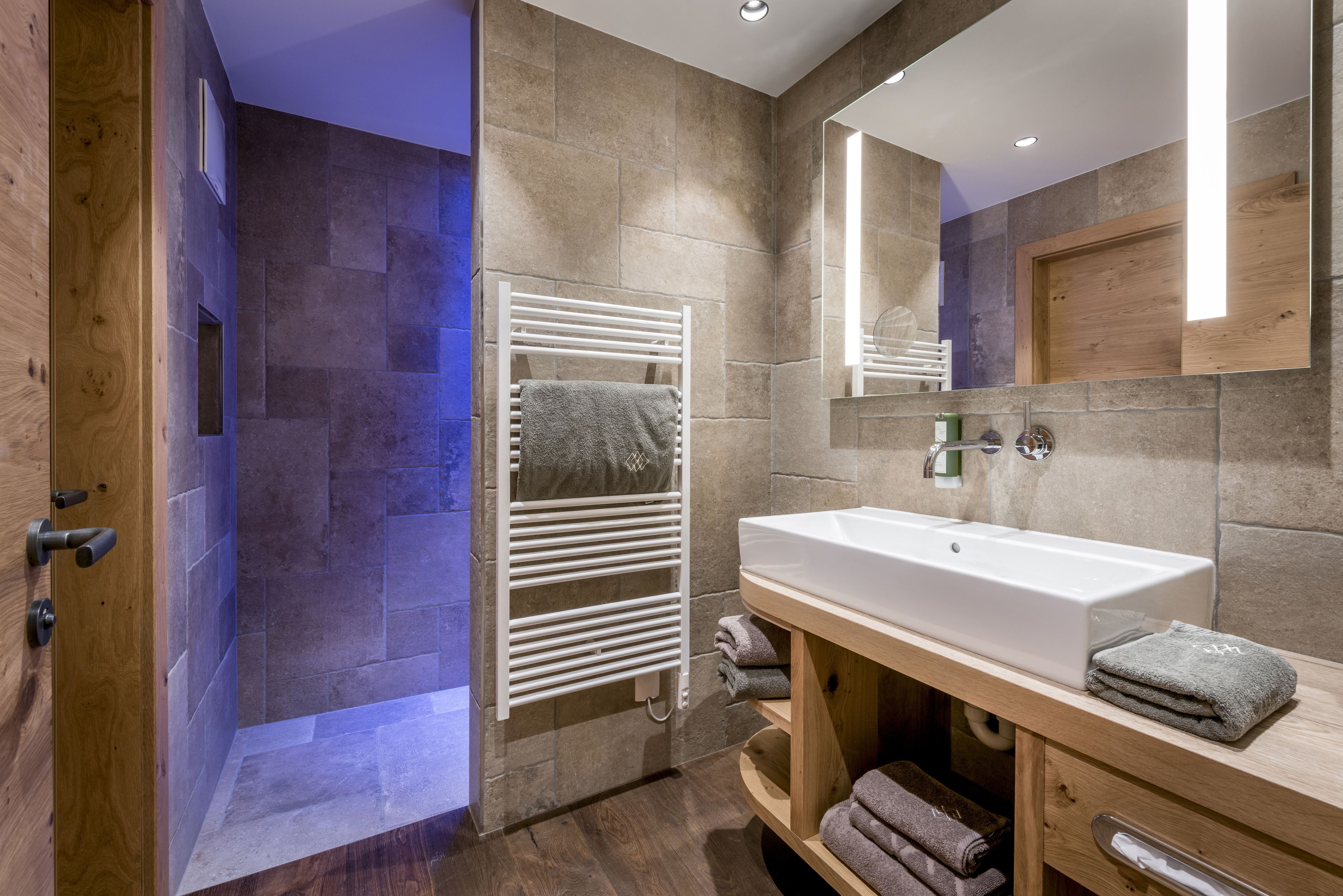 A modern bathroom with a shower, a white sink, and a wooden vanity.