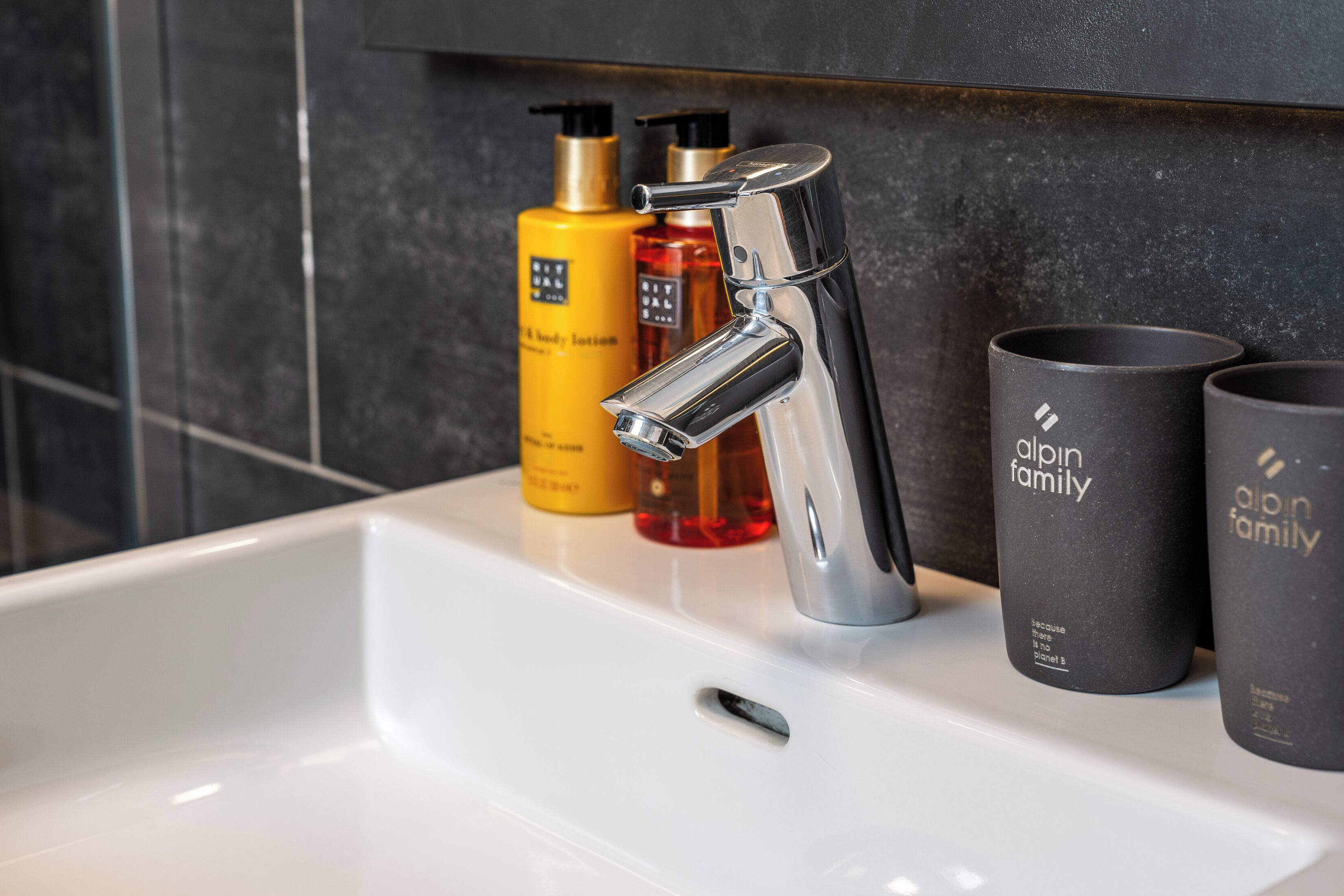 A bathroom sink with a chrome faucet, two yellow bottles, and two black cups with text.