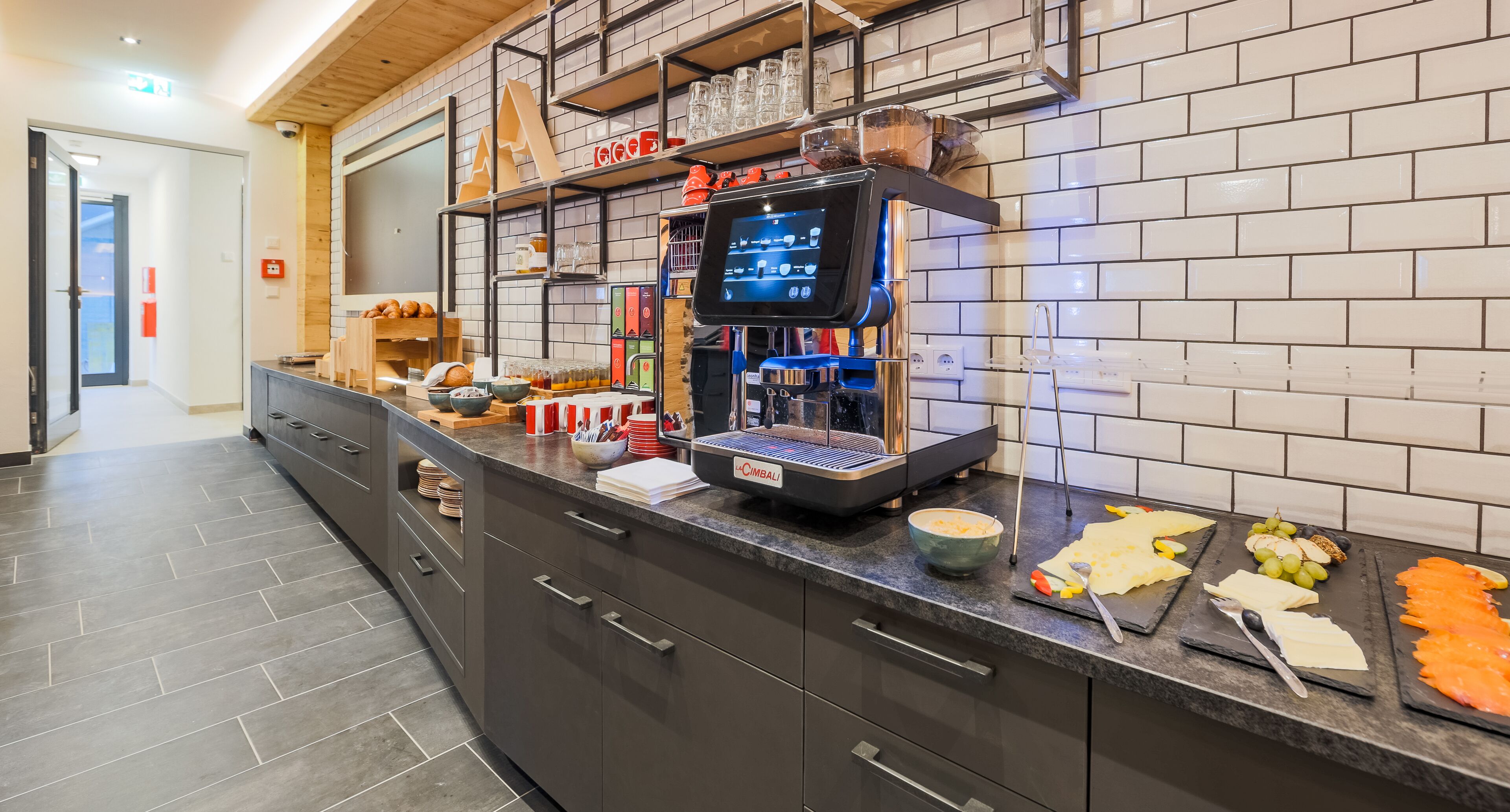 Een moderne keuken met een bedieningspunt, inclusief een koffieapparaat, diverse etenswaren en een digitaal scherm.