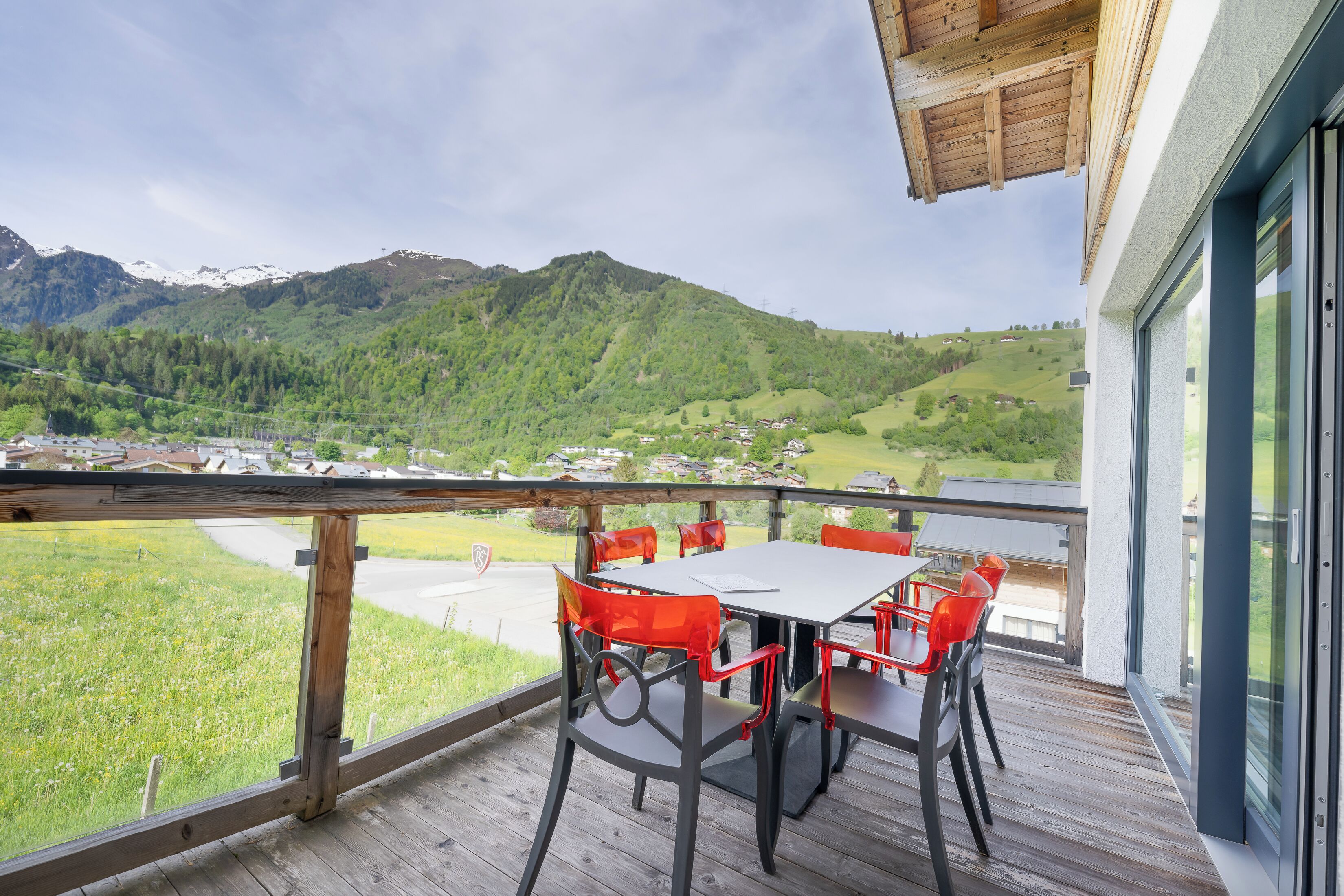 A balcony with a table and chairs, overlooking a mountainous landscape with houses in the distance.