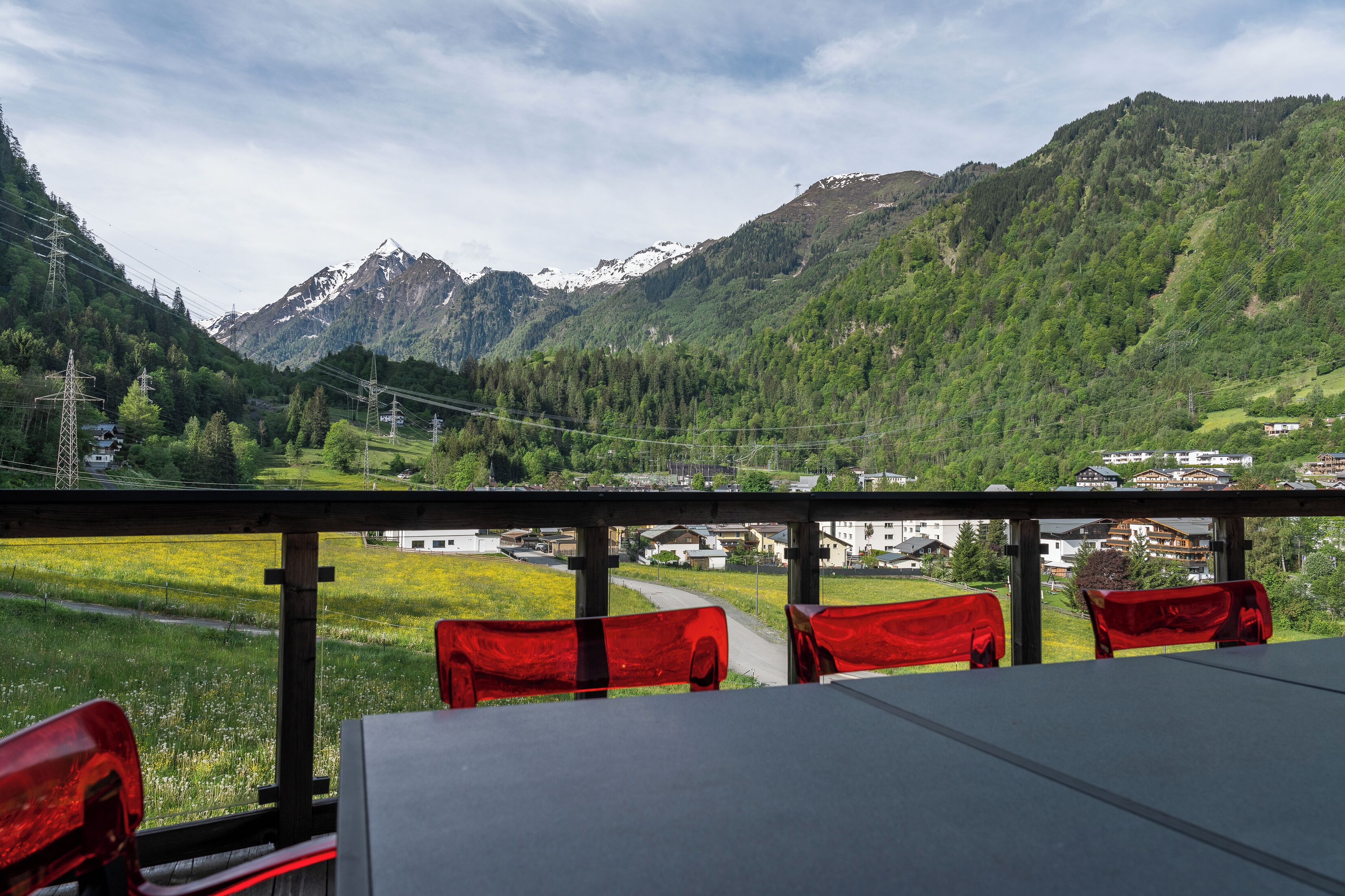 Restaurante com vista para a montanha, cadeiras vermelhas e uma mesa.