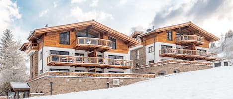 Un chalet de varios pisos con balcones de madera y una pista de esquí al fondo.