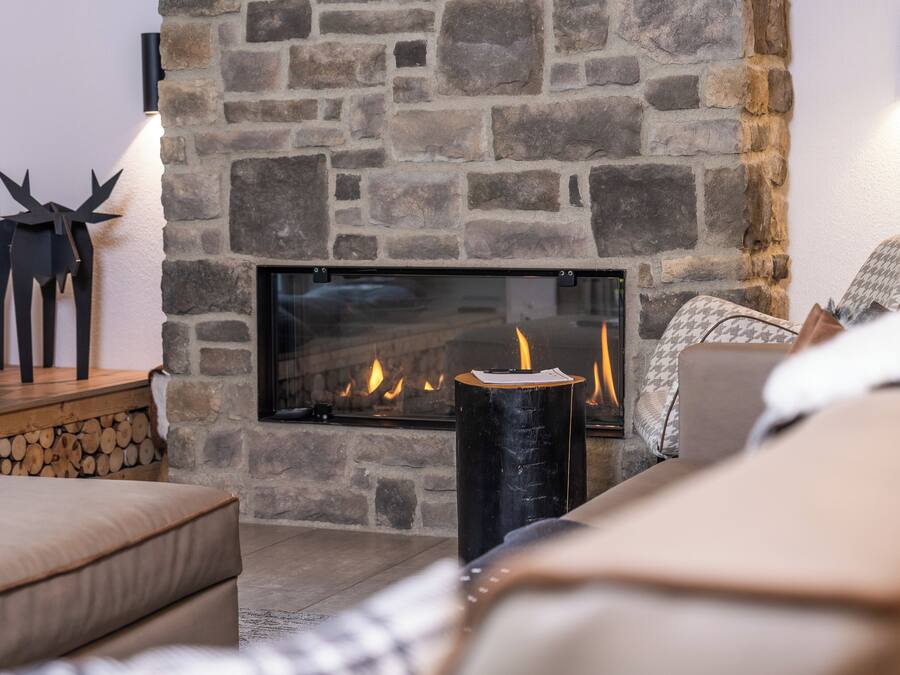 A cozy living room with a stone fireplace, a log stack, and a modern sofa.