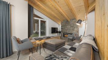 A cozy living room with a stone fireplace, wooden ceiling beams, and a comfortable seating area.