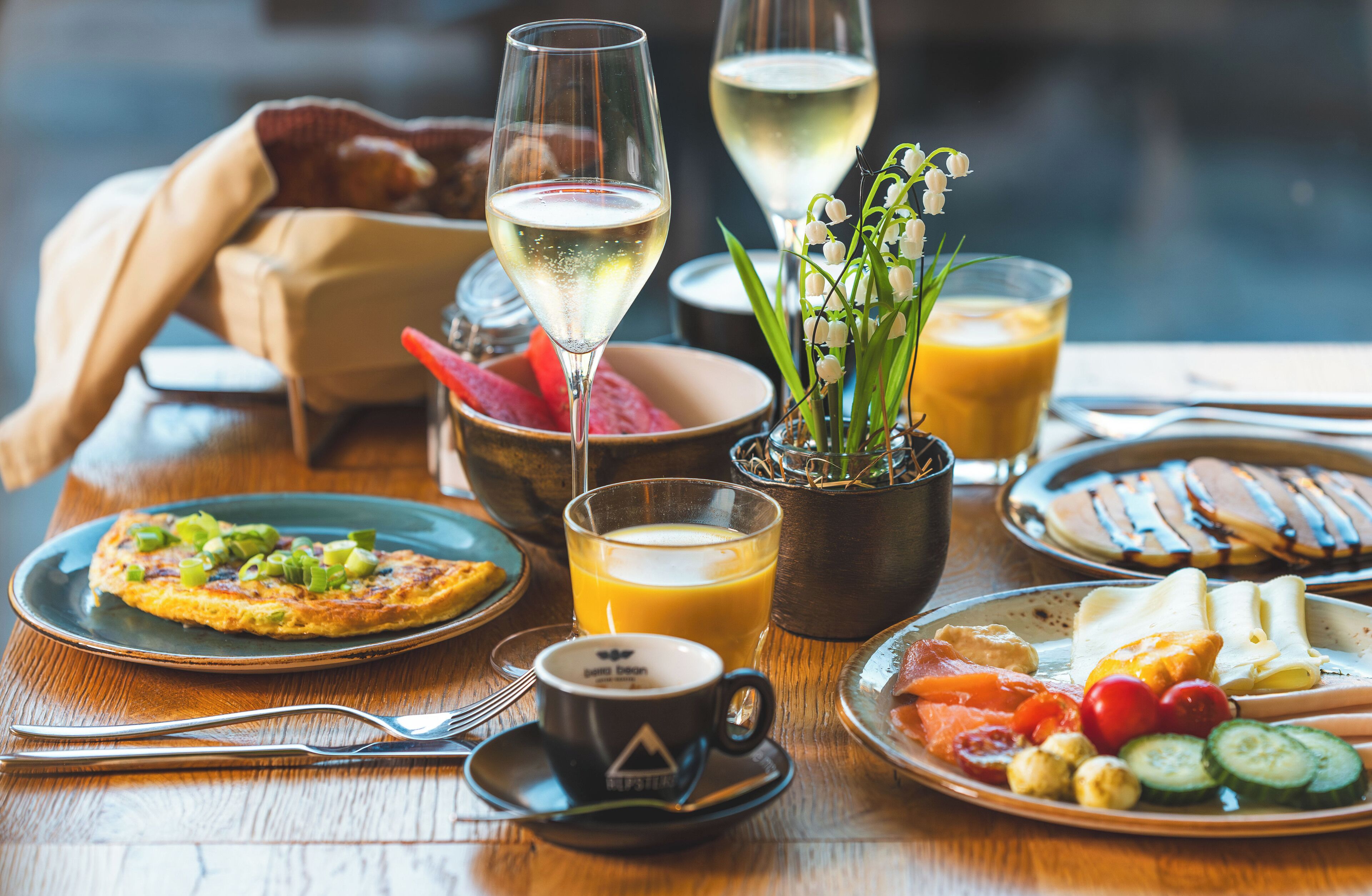 A breakfast setting with a plate of food, a glass of orange juice, a cup of coffee, and a glass of white wine.