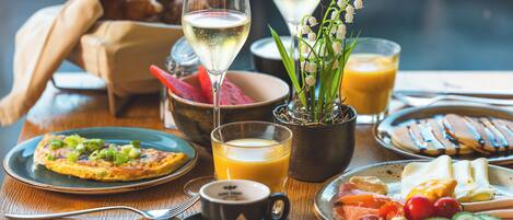 Un desayuno con un plato de comida, un vaso de jugo de naranja, una taza de café y una copa de vino blanco.