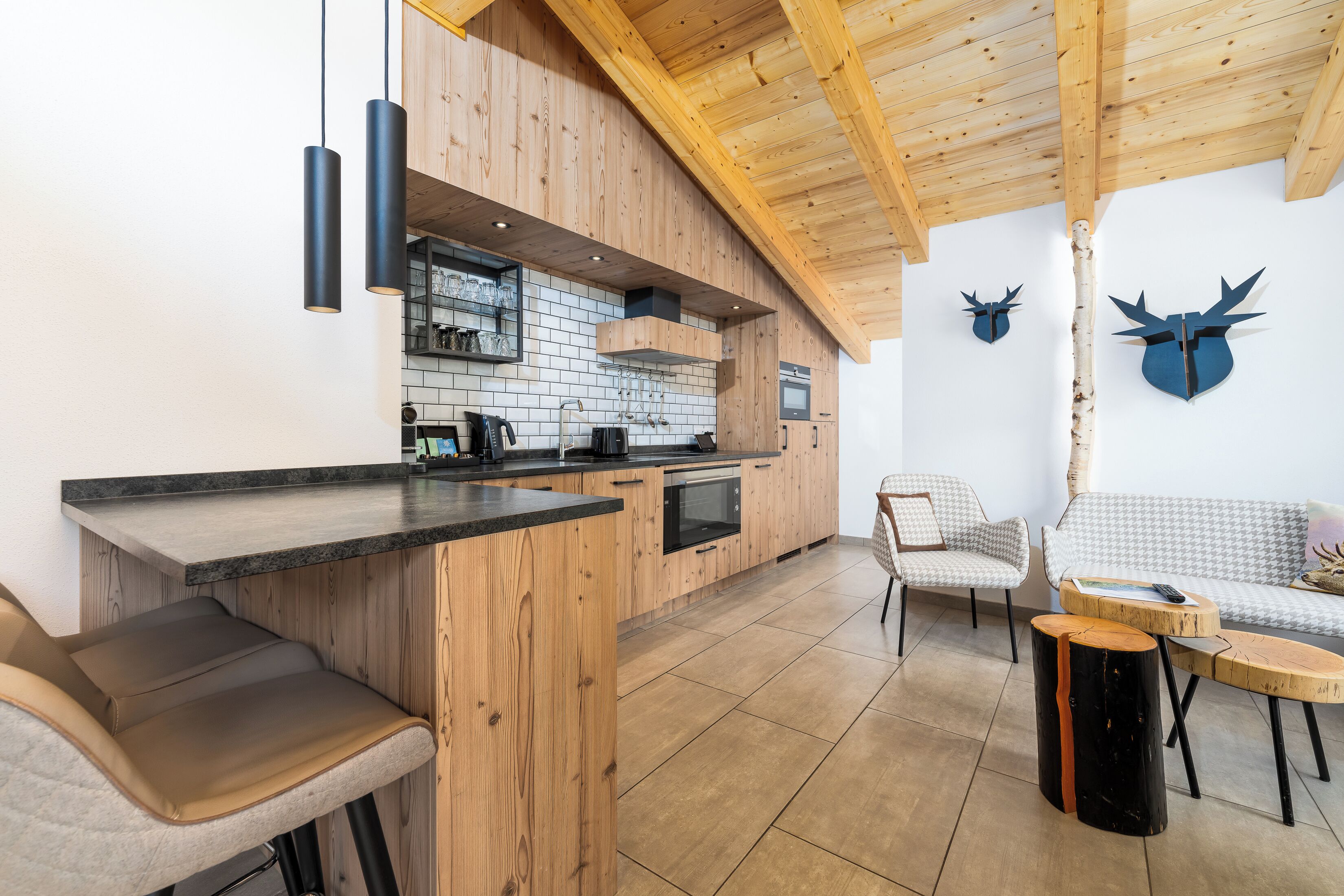 A modern kitchen with wooden cabinetry, a black countertop, and a built-in oven. There are two chairs and a small table with a vase.