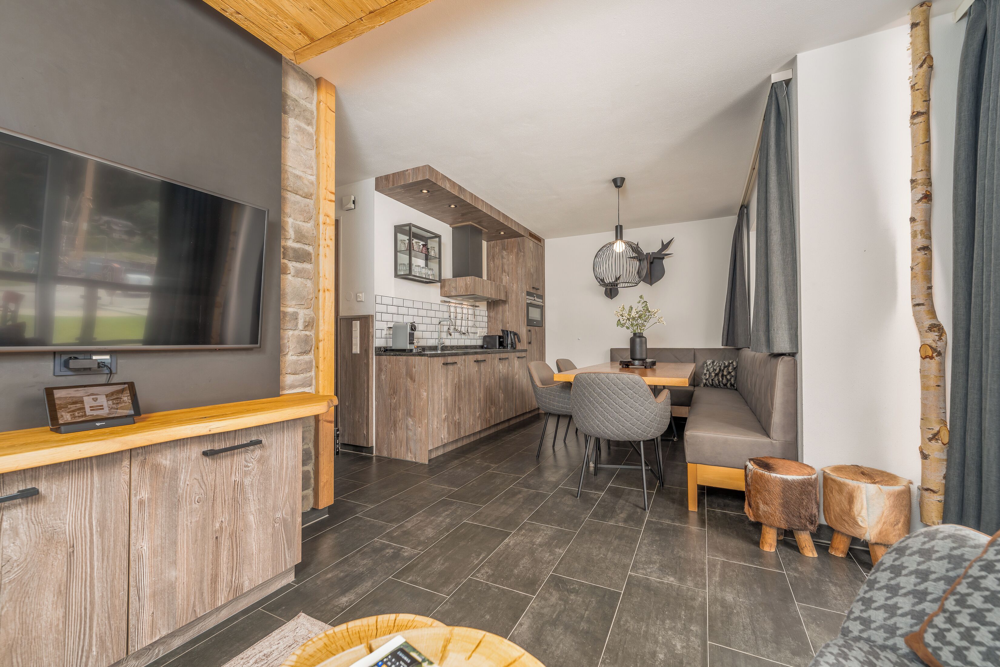 A modern kitchen with a large TV, wooden cabinets, and a dining area with a sofa and chairs.