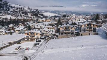 Un pueblo cubierto de nieve con edificios, incluyendo un hotel de varios pisos y balcones, y una carretera con vehículos.