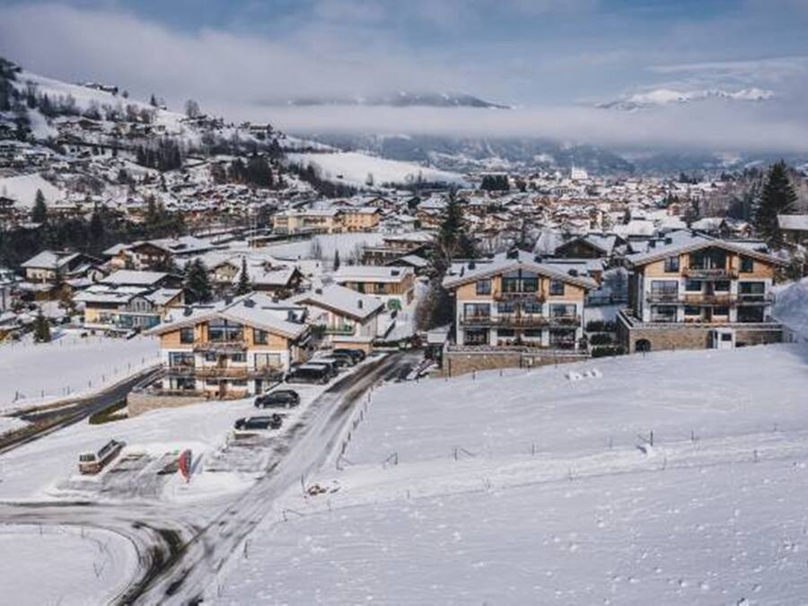 Un pueblo cubierto de nieve con edificios, incluyendo un hotel de varios pisos y balcones, y una carretera con vehículos.