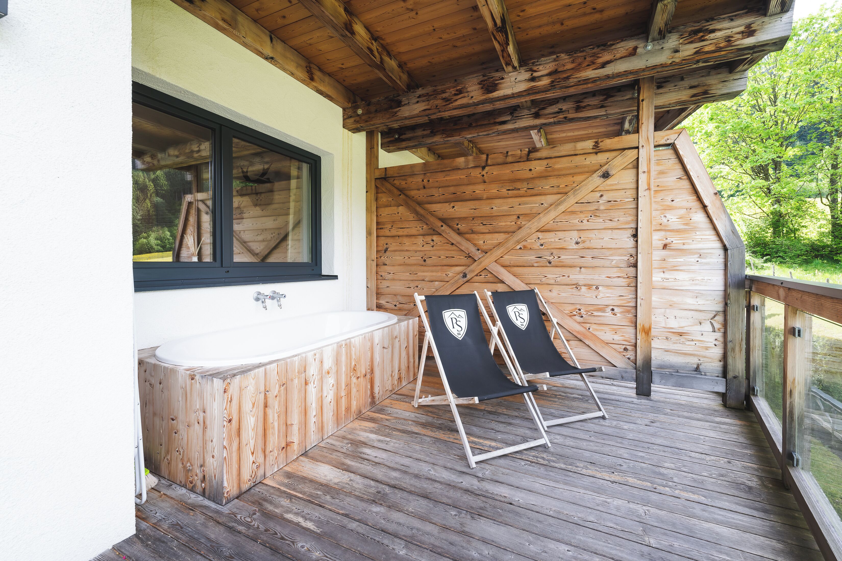 A wooden deck with a hot tub and two lounge chairs.