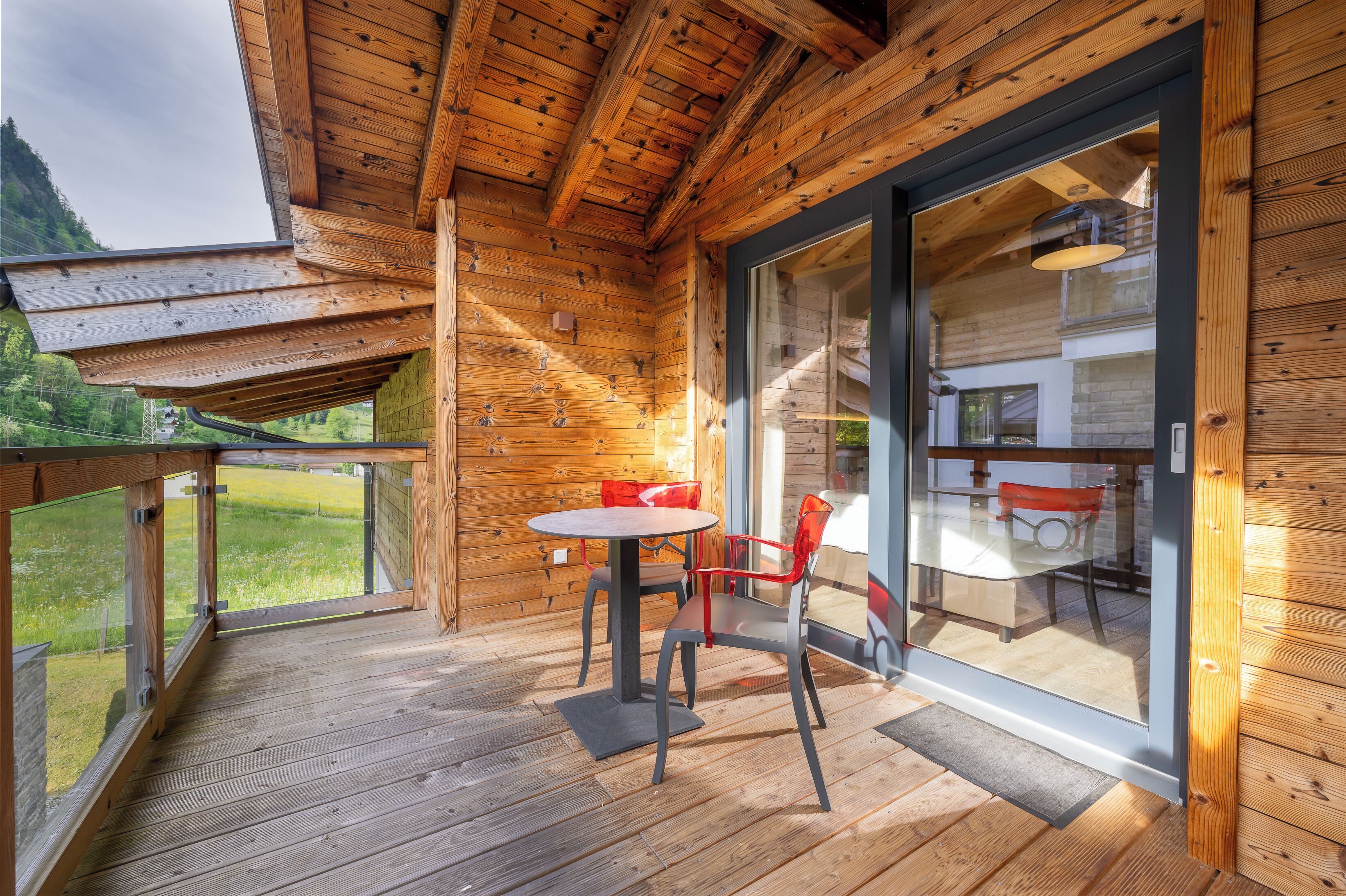 A wooden deck with a table and chairs, a glass door leading inside, and a view of a mountain.