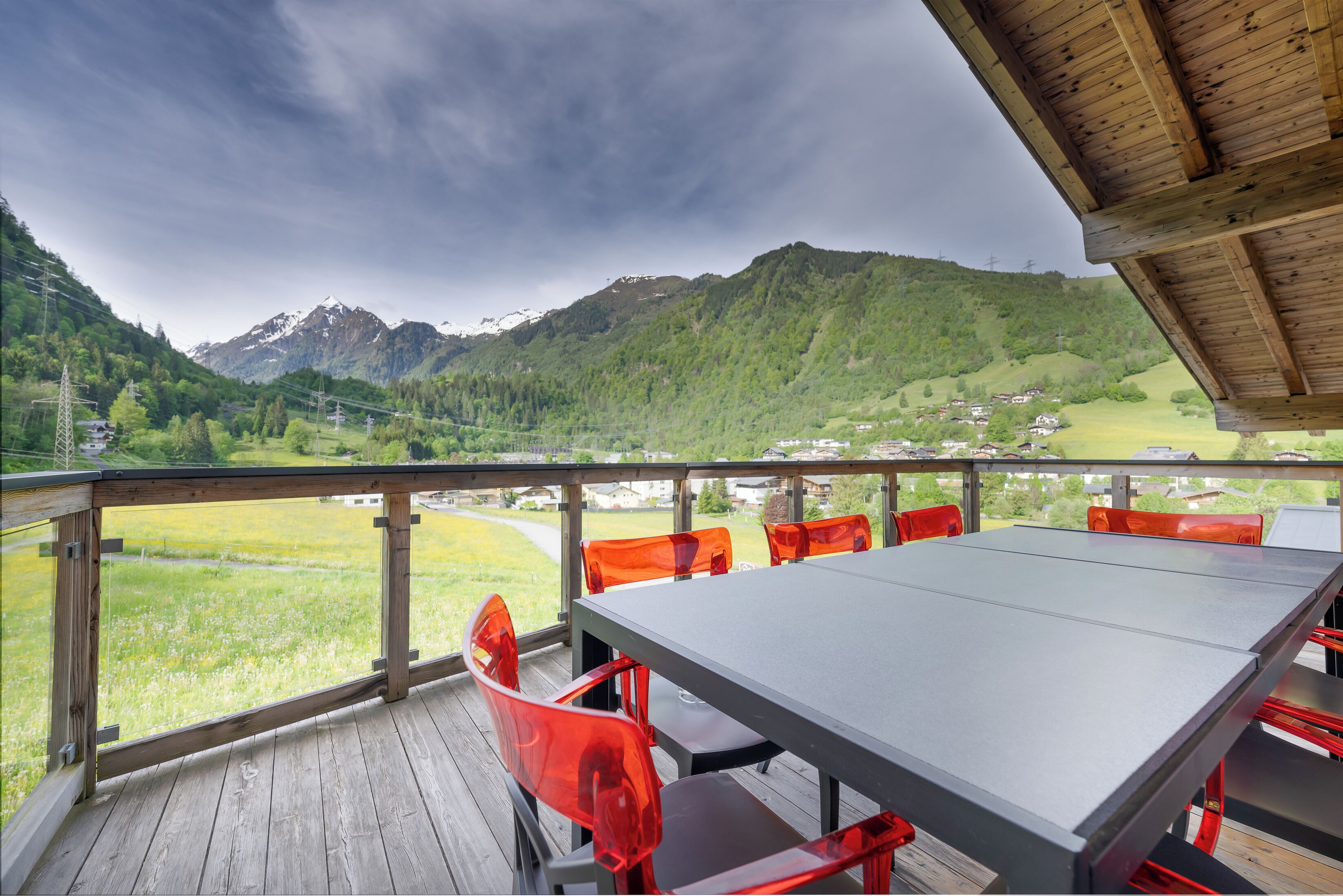 En træterrasse med et bord og røde stole, der kigger ud over et bjerglandskab.