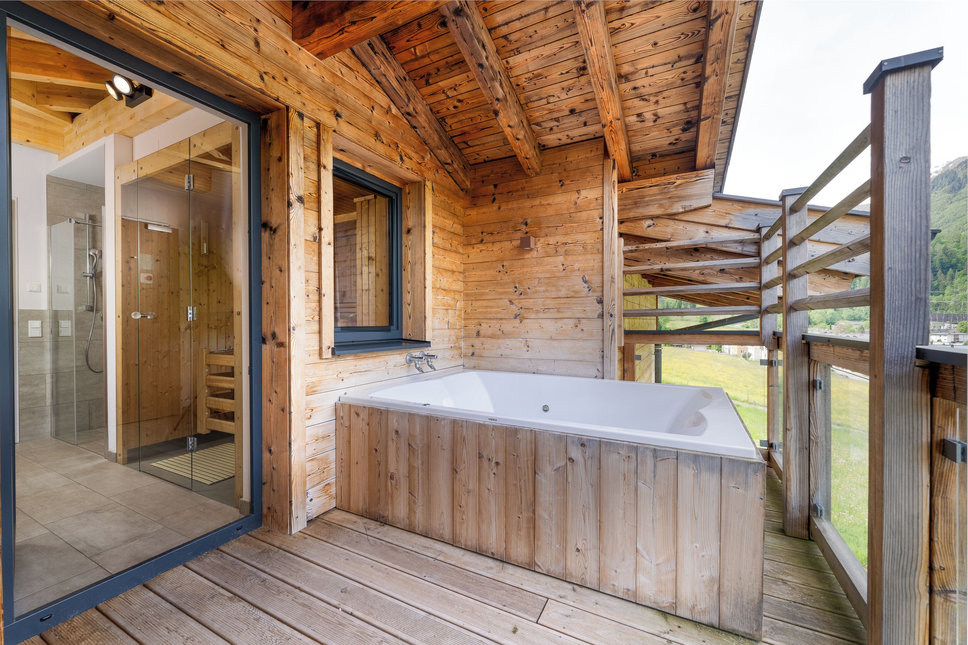 Una cabaña de madera con ducha envuelta en vidrio, terraza de madera y jacuzzi.