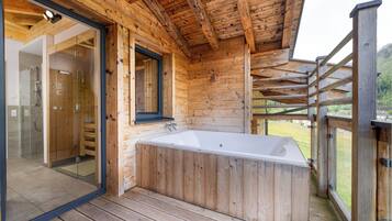 Una cabaña de madera con ducha envuelta en vidrio, terraza de madera y jacuzzi.