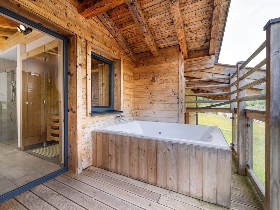 Una cabaña de madera con ducha envuelta en vidrio, terraza de madera y jacuzzi.