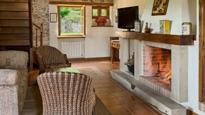 A cozy living room with a fireplace, wooden beams, and a television. - Apartamentos Llugarón (Villaviciosa)
