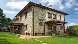 A stone house with a patio, outdoor seating, and a garden. - Apartamentos Llugarón (Villaviciosa)