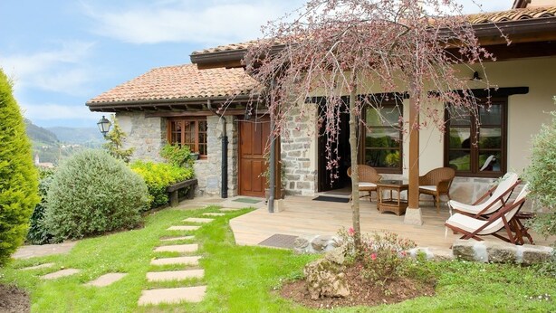 A stone house with a tiled roof, a garden with stepping stones, and outdoor seating. - Apartamentos Llugarón (Villaviciosa)