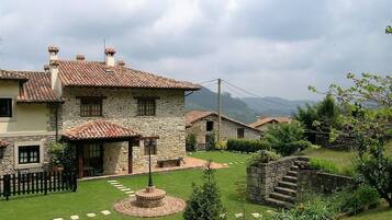 A stone house with a tiled roof, a circular garden feature, and a stone staircase.