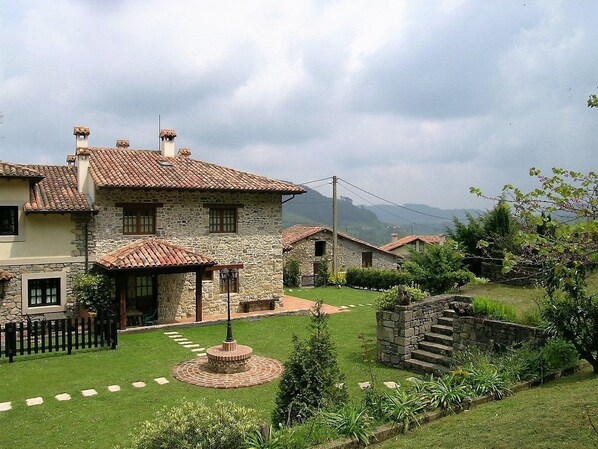 Una casa de piedra con techo de tejas, un jardín circular y una escalera de piedra.
