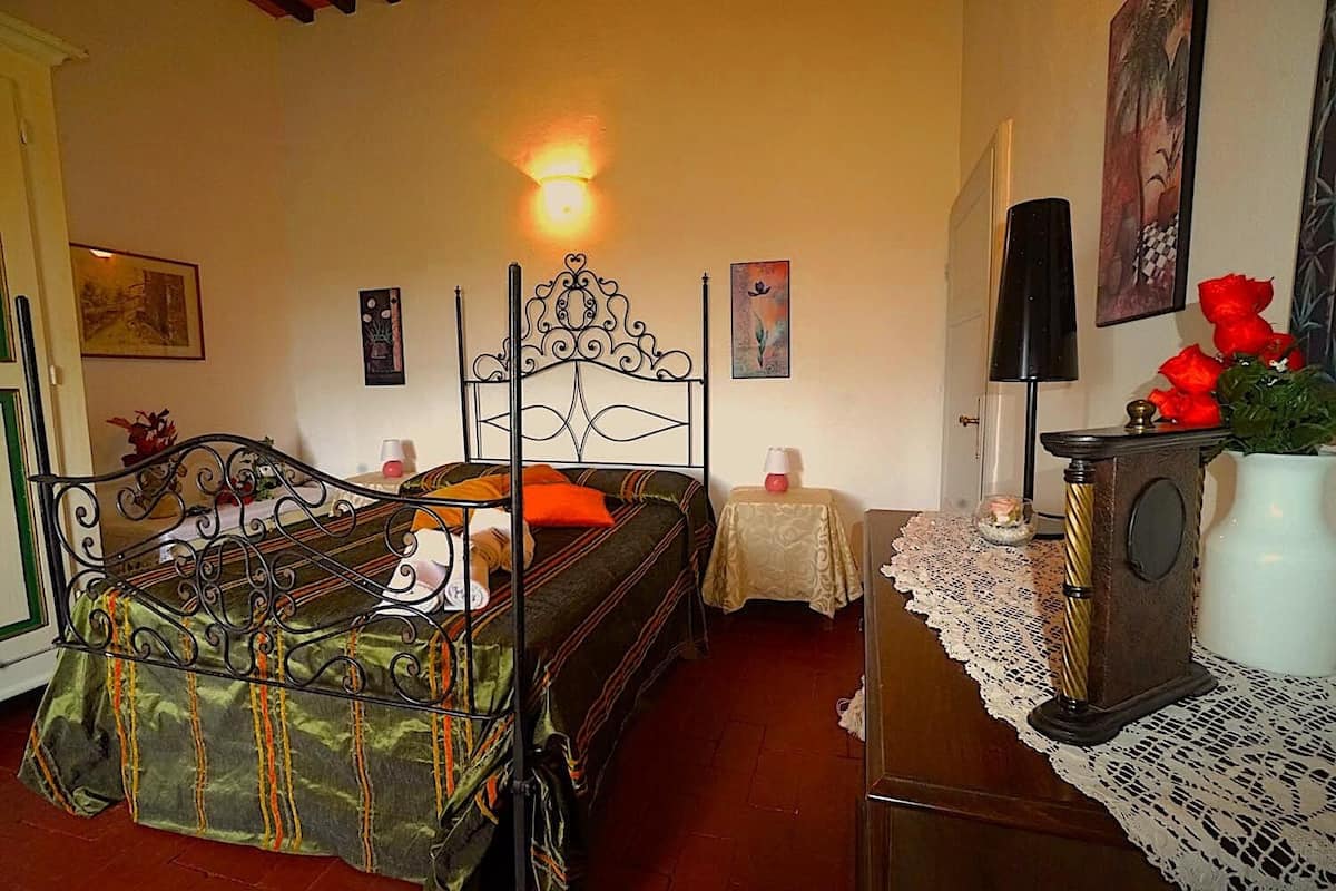 A room with a bed, a table with a vase of flowers, and a wall-mounted lamp.