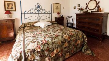 Une chambre à coucher avec une couvre-lit à motifs floraux, une commode en bois, une chaise et une table de chevet avec une lampe.