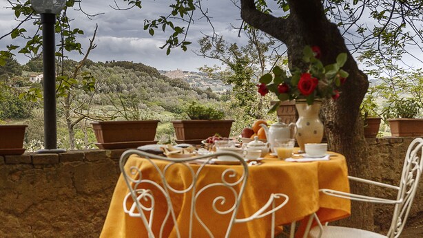 An outdoor dining area with a table set for two, surrounded by terracotta pots and a view of a hillside. - Locanda Etrusca (Bibbona)