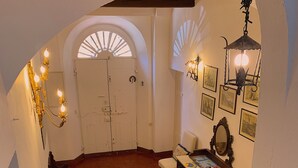A room with a large rug, a wooden bench, a table with magazines, a wall-mounted mirror, and a door with a white frame. - Locanda Etrusca (Bibbona)