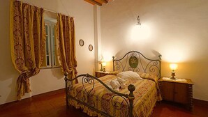 A bedroom with a bed, two bedside tables, a window with curtains, a wall clock, and a ceiling light fixture. - Locanda Etrusca (Bibbona)