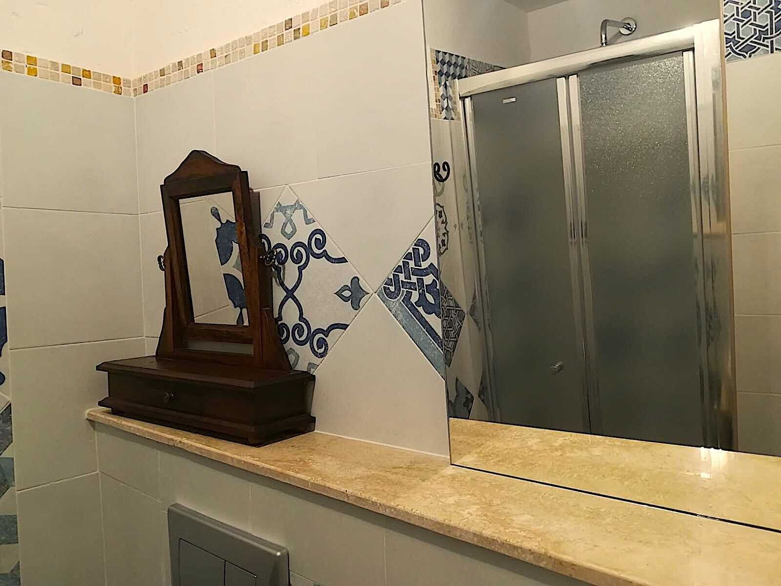 Casa de banho com espelho, cabine de duche e azulejos decorativos.