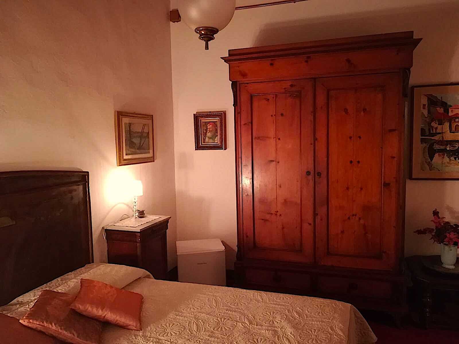 Un dormitorio con una cama, un armario de madera, una mesita de noche con una lámpara y cuadros en la pared.
