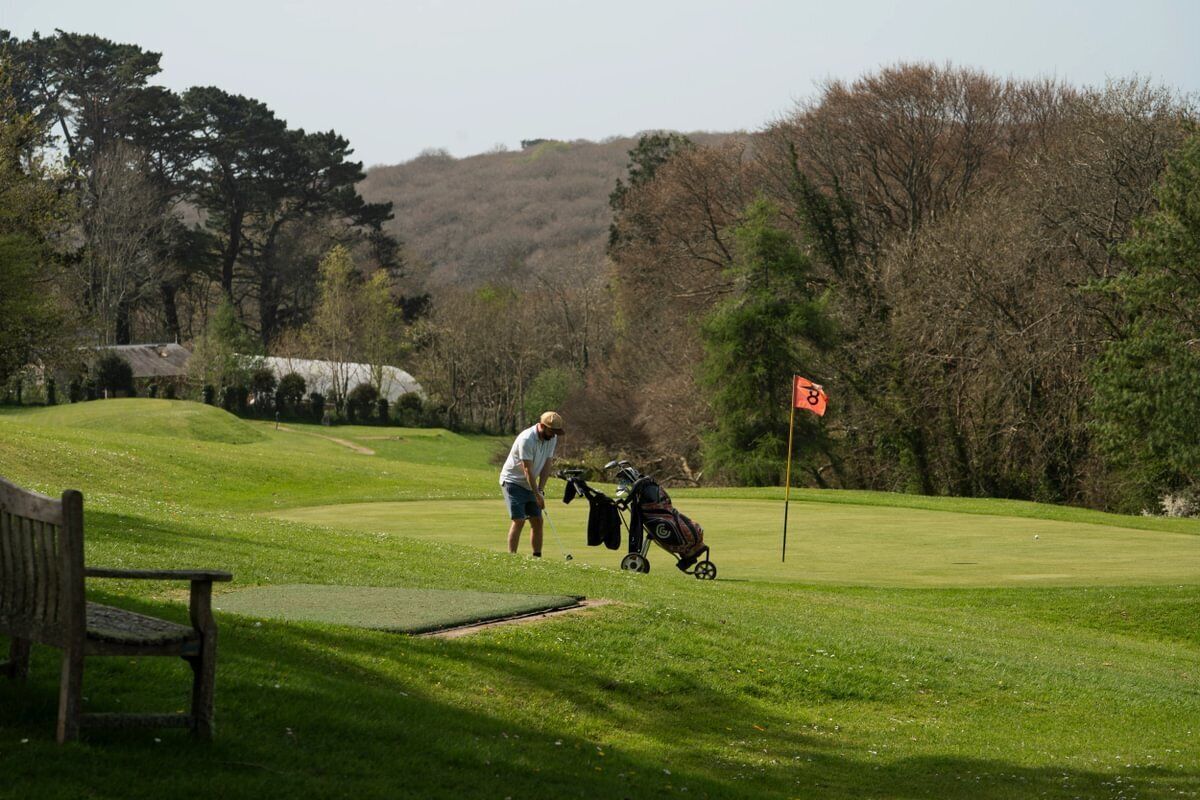 A golf course with a flagstick, a golf bag, and a bench.