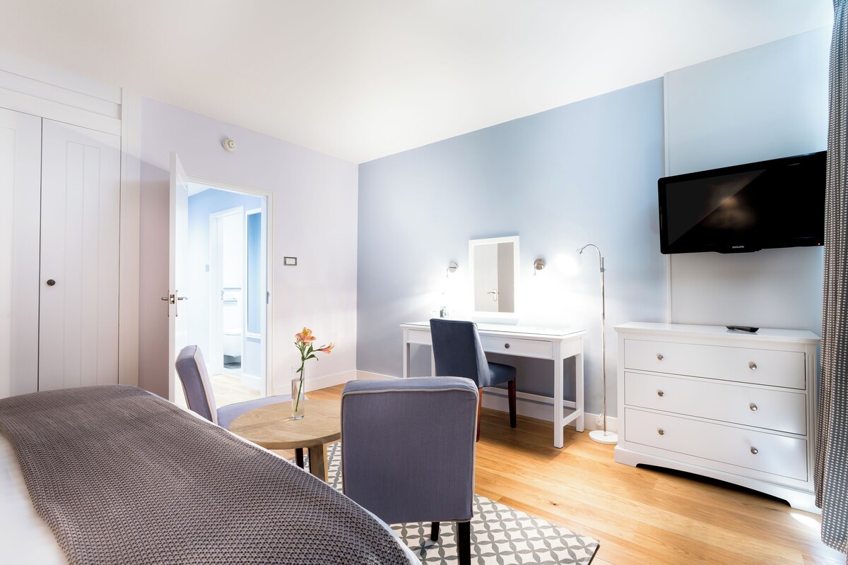 A modern bedroom with a bed, a desk, a chair, a dresser, and a TV.