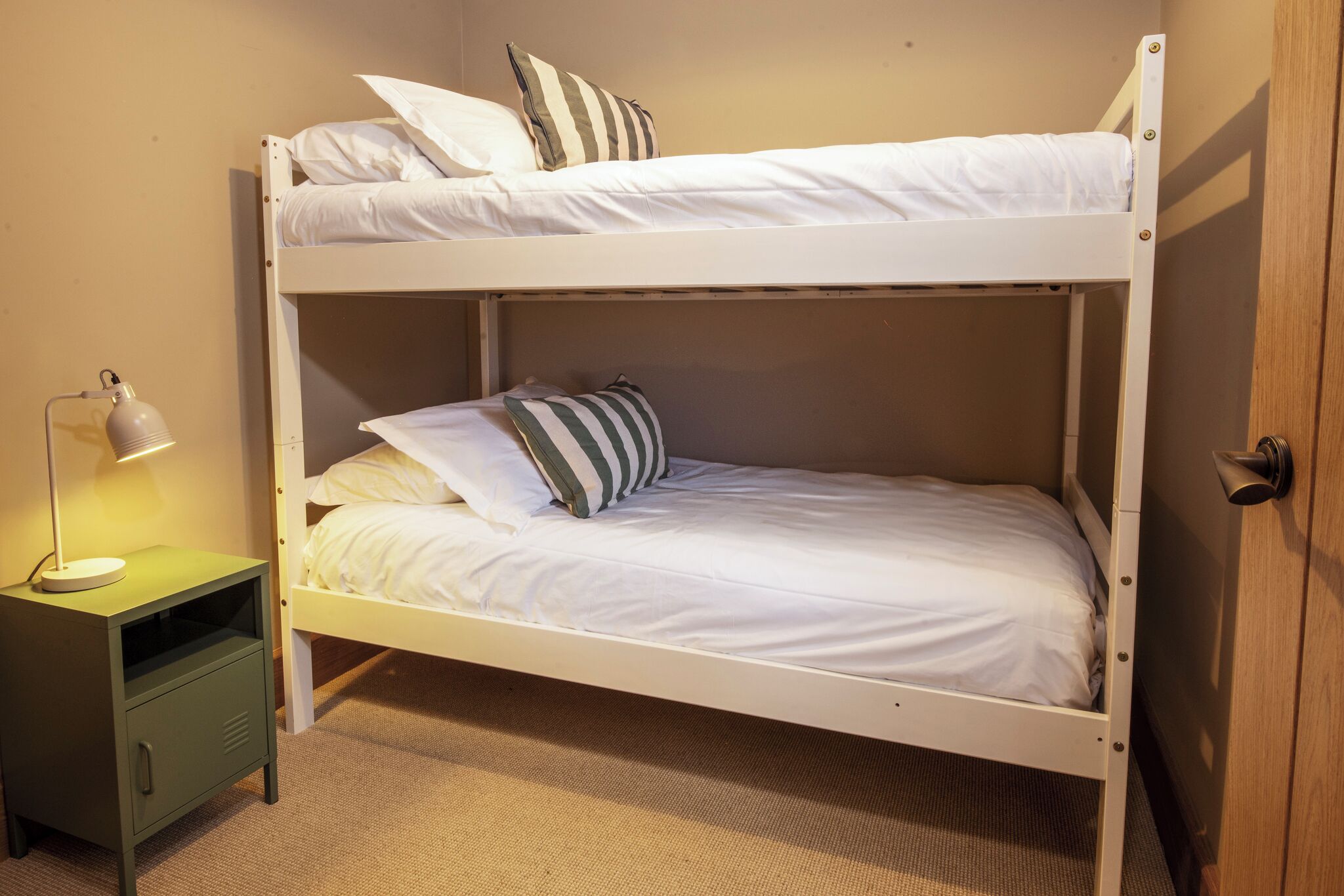 Una cama individual con ropa de cama blanca, una lámpara de noche y una mesita de noche verde.