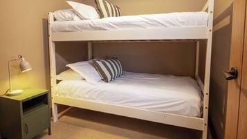 Una cama individual con ropa de cama blanca, una lámpara de noche y una mesita de noche verde.