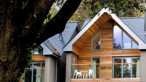 Ein modernes Haus mit einer Stein-Fassade, großen Fenstern und einer Holzterrasse mit Sitzgelegenheiten.